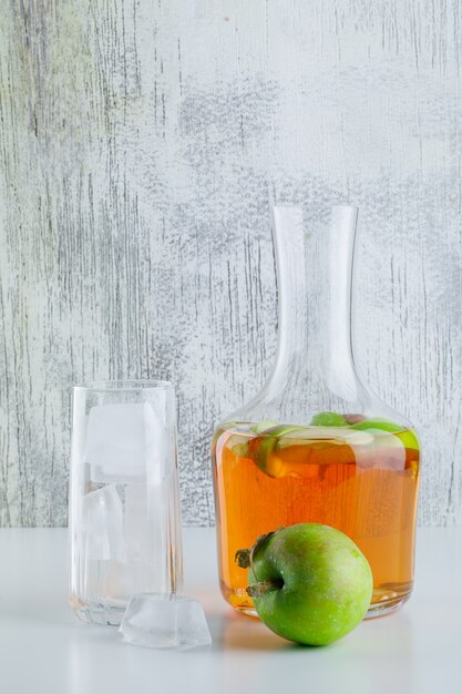 Apple with drink, ice cubes in glass on white and grungy, side view.