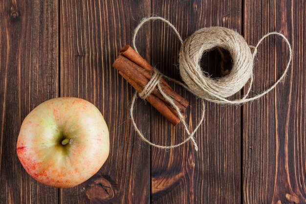 An apple with dry cinnamon and rope top view on a wooden background