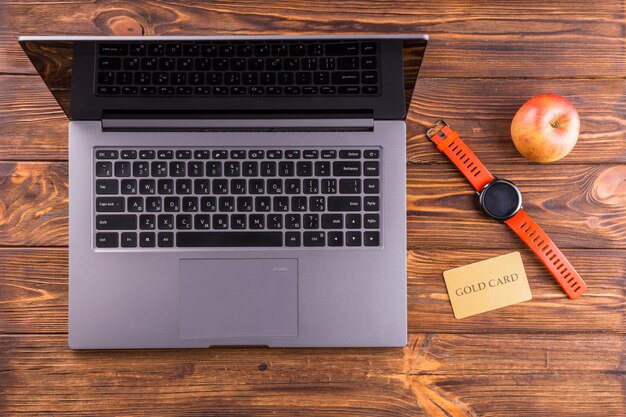 Apple; wristwatch; laptop and gold card on wooden desk