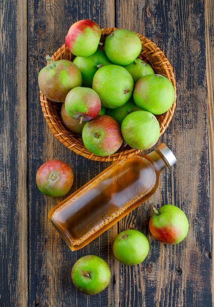 Apples in a basket with bottle of drink top view on a wooden background