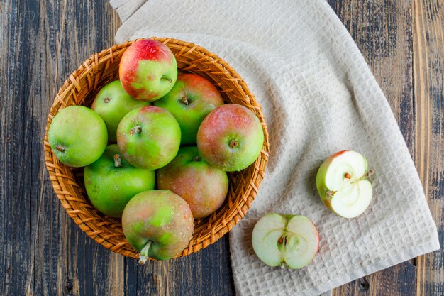 Яблоки в корзине на фоне деревянных и кухонных полотенец. плоская планировка.