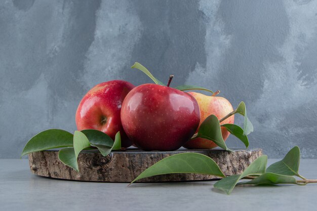 Яблоки и листья сложены на деревянной доске по мрамору.
