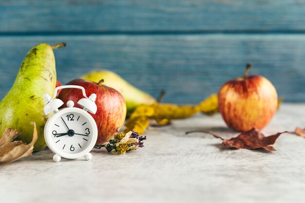 目覚まし時計の近くのリンゴとナシ