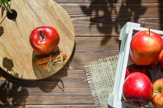 Яблоки в белой коробке и яблоко с палочками корицы на разделочной доске
