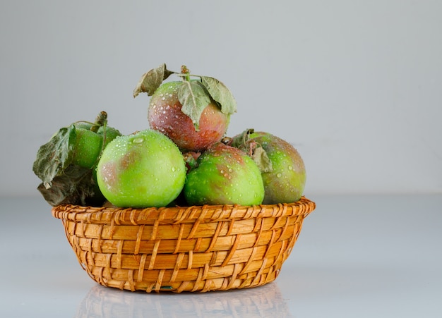 Яблоки в плетеной корзине с листьями, вид сбоку на белом градиенте