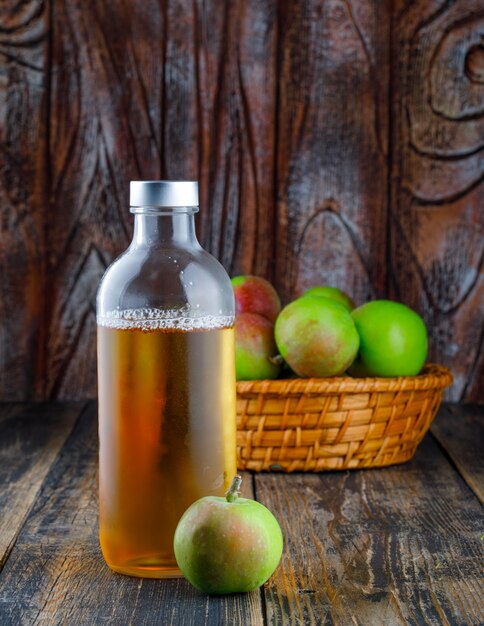 Apples with bottle of drink in a basket on wooden background, side view.