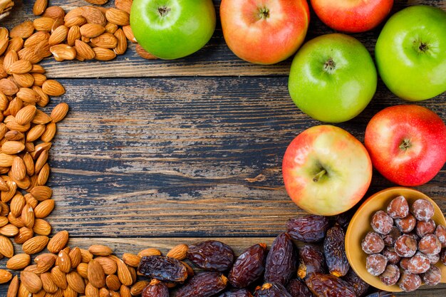 Apples with dates, almonds and nuts in wooden spoon on old wooden background, flat lay.