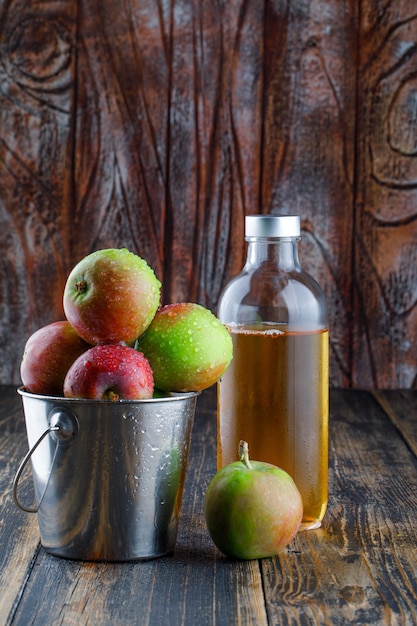 Apples with drink in a mini bucket on old wooden background, side view.