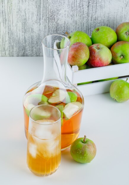 Apples with drinks in a wooden box on white and grungy, high angle view.