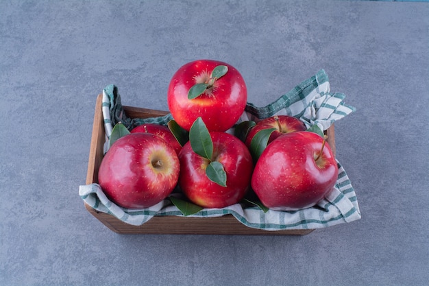 Apples with leaves on towel on a box on the dark surface