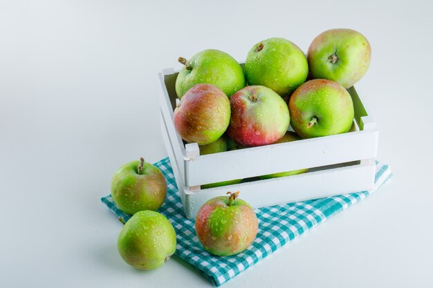 Apples in a wooden box on white and picnic cloth. high angle view.