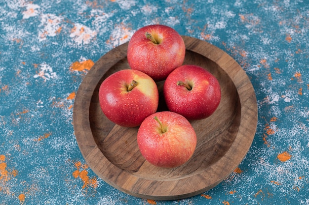 Apples in a wooden plate on a blue texture table.