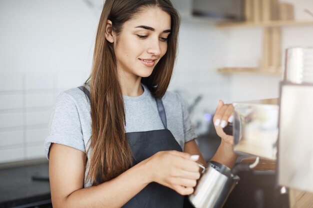 Apprentice lady barista learning how to skim milk in a jug on her first day on a new job