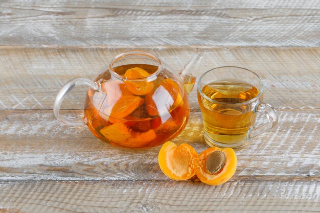 Apricot tea in teapot and glass mug with apricots top view on a wooden table