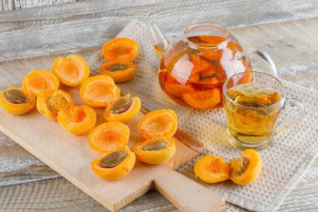 Apricot tea in teapot and mug with apricots, cutting board top view on wooden and kitchen towel