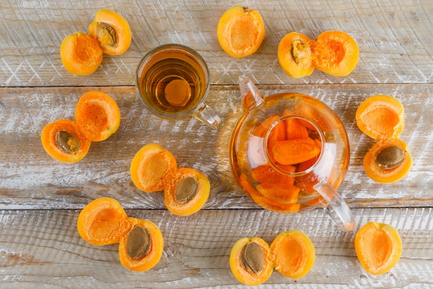 Free photo apricot tea with apricots in teapot and glass mug on wooden table, flat lay.