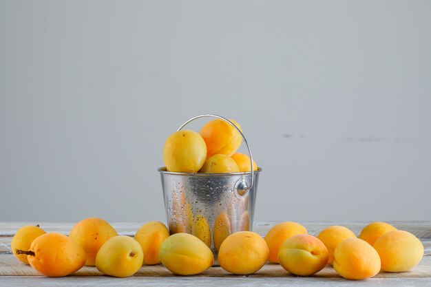 Apricots in a mini bucket on wooden table, side view.