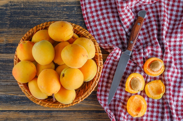 Apricots in a wicker basket with knife flat lay on picnic cloth and wooden table