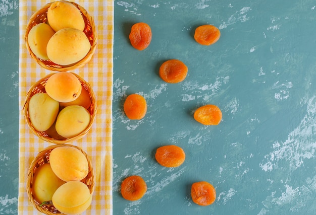 Free photo apricots with dried apricots in baskets on plaster and picnic cloth, top view.