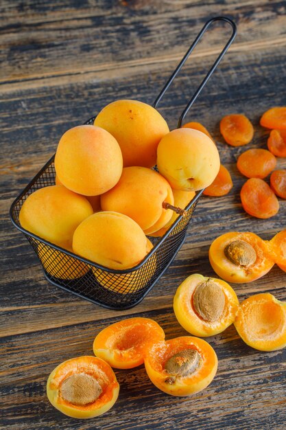 Apricots with dried apricots in a colander on wooden table, top view.