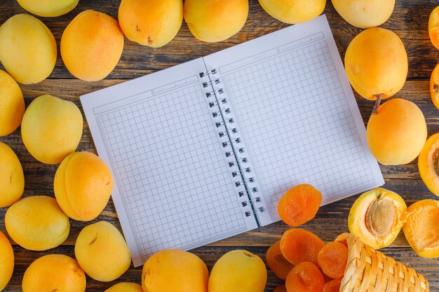 Apricots with dried apricots, opened notebook on wooden table, flat lay.