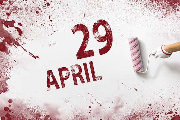 4​月​29​日​。​月​の​29​日​、​カレンダー​の​日付​。​手​は​赤い​ペンキ​で​ローラー​を​保持し​、​白い​背景​に​カレンダー​の​日付​を​書き込みます​。​春​の​月​、​年​の​日​の​概念​。