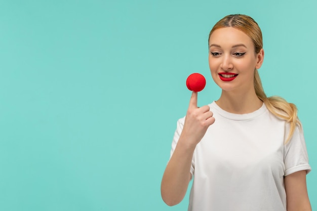 April fools day blonde smiling girl pony tail red nose on top of finger white tshirt clown funny