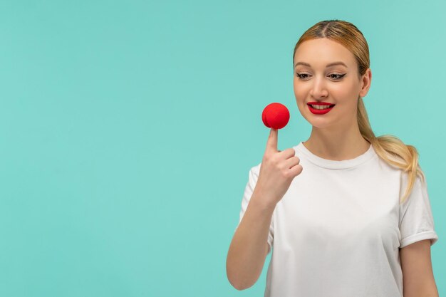 April fools day blonde smiling girl pony tail red nose on top of finger white tshirt clown funny