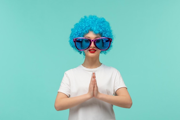 Pesce d'aprile pagliaccio che prega ragazza mani insieme grandi occhiali da sole blu costume divertente capelli blu