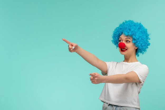 April fools day excited girl directing left with red nose in a clown costume blue hair