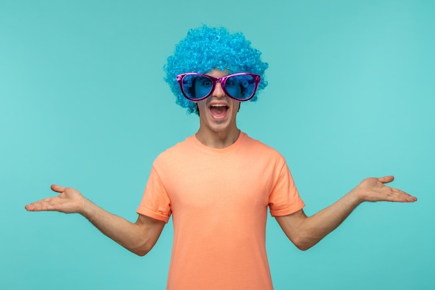 Бесплатное фото День дурака парень клоун счастливый голубые волосы розовые большие солнцезащитные очки руки машут удивленно смешно