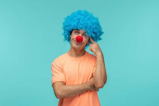 April fools day ragazzo clown occhi roteanti toccando la testa tempie capelli blu mani incrociate divertente naso rosso