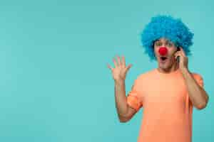 Free photo april fools day guy clown surprised holding phone blue hair hands up excited funny red nose