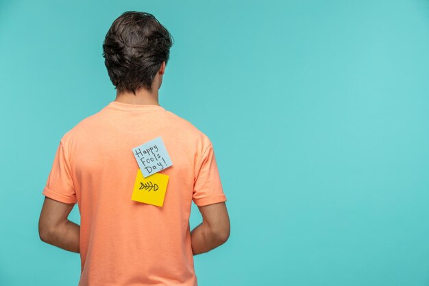 April fools day guy from behind blue and yellow post it sticker note on orange tshirt fish skeleton