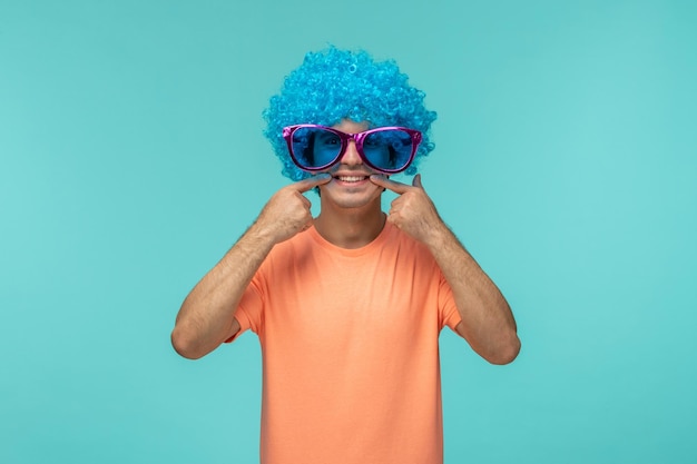 Free photo april fools day happy guy clown funny blue hair blue pink big sunglasses fingers pointing at mouth