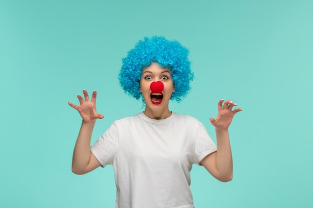 April fools day scaring girl catching hands pose with red nose in a clown costume blue hair