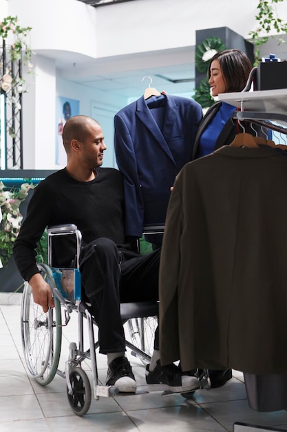 Бесплатное фото Арабский клиент в инвалидной коляске общается с продавцом, обсуждает куртки, доступные в магазине одежды. клиент с инвалидностью изучает стиль и размер одежды во время покупок формального наряда