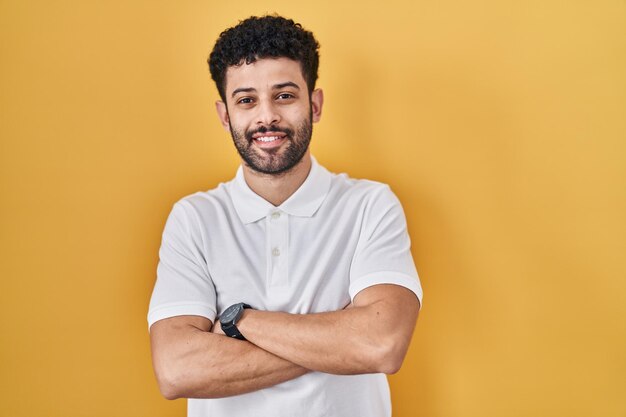 Arab man standing over yellow background happy face smiling with crossed arms looking at the camera. positive person.