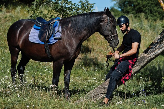 アラブの背の高いひげの男は、アラビアの馬と黒のヘルメットを着用