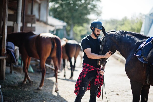 Арабский высокий бородатый мужчина в черном шлеме с арабской лошадью