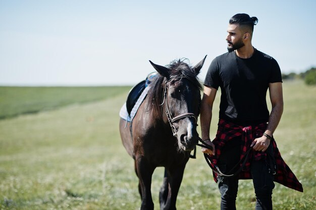 アラブの背の高いあごひげの男は、アラビアの馬と黒で着用