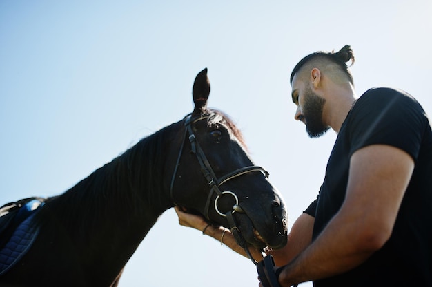 アラブの背の高いあごひげの男は、アラビアの馬と黒で着用