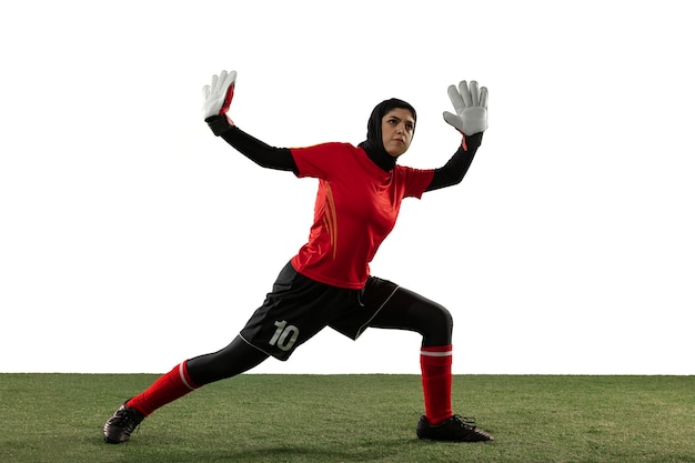 Arabian female soccer or football player, goalkeeper on white studio background. Young woman catching ball, training, protecting goals in motion and action. Concept of sport, hobby, healthy lifestyle.