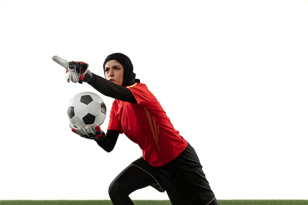 Arabian female soccer or football player, goalkeeper on white studio background. Young woman giving pass, emotional gesturing, protecting goals for team. Concept of sport, hobby, healthy lifestyle.