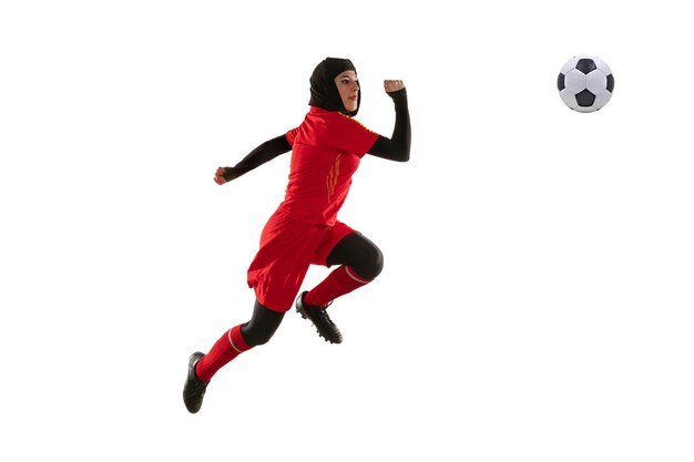 Arabian female soccer or football player isolated on white studio background. Young woman kicking ball in jump, catched in air, training in motion, action. 