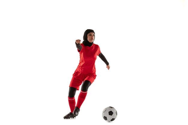 白いスタジオの背景に分離されたアラビアの女性サッカーまたはサッカー選手。ボールを蹴り、トレーニングし、動きと行動の練習をしている若い女性。