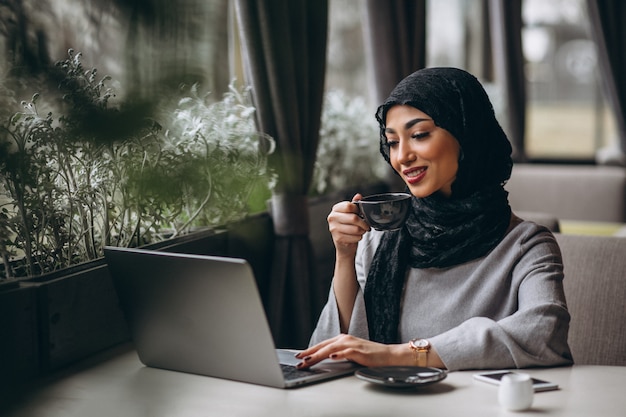ラップトップに取り組んでいるカフェの中のヒジャーブのアラビア女性