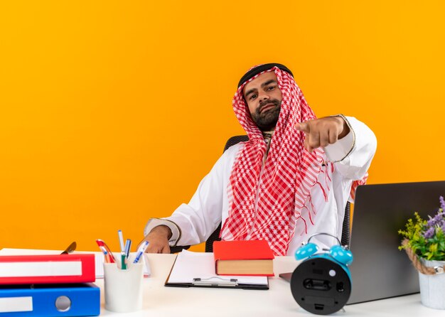 Arabic businessman in traditional wear sitting at the table pointing with finger  working in office