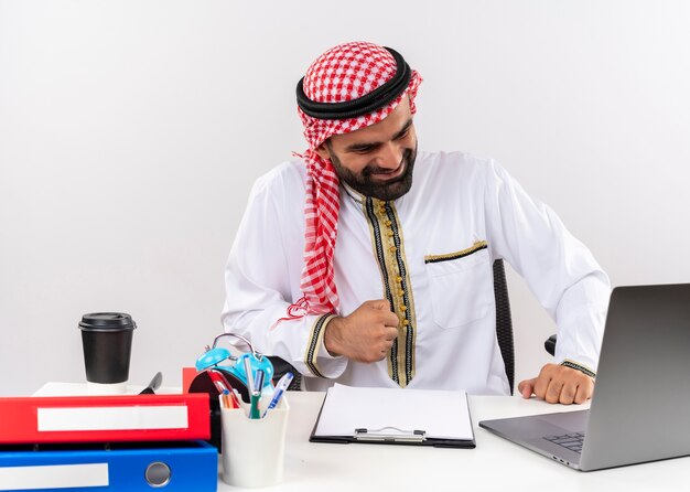 노트북 컴퓨터가 주먹을 행복 떨림으로 테이블에 앉아 전통적인 착용 아랍어 사업가 사무실에서 일을 종료