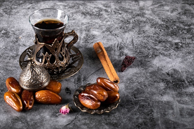 Arabic delight dates on a dark marble with a glass of tea and some cinnamon sticks